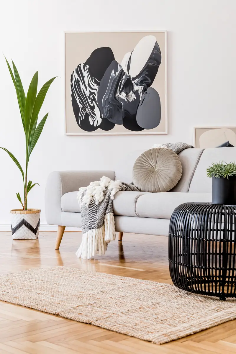 Staged living room with a light grey sofa, framed abstract art, jute rug and a black rattan coffee table