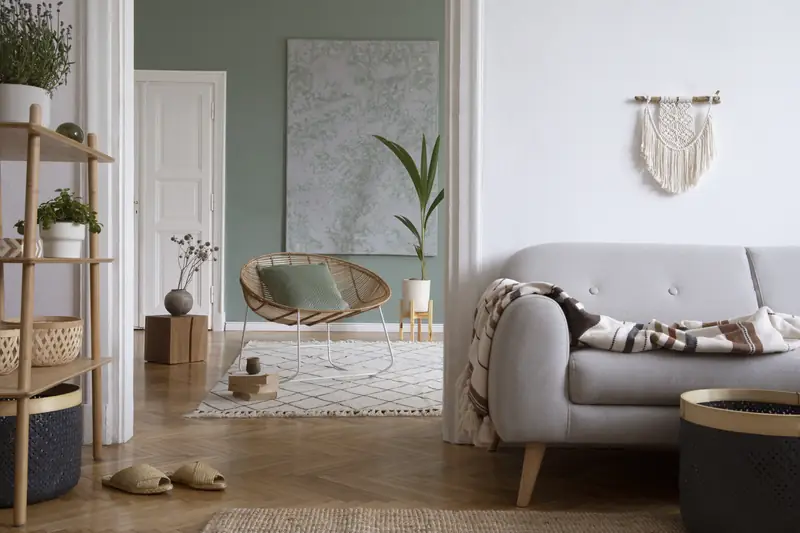 Staged sitting area with a rattan lounge chair, sage green accent wall and herringbone wood floors