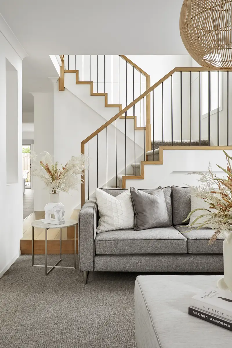 Staged entry lounge with a grey sofa, marble side table, dried florals and an open oak staircase